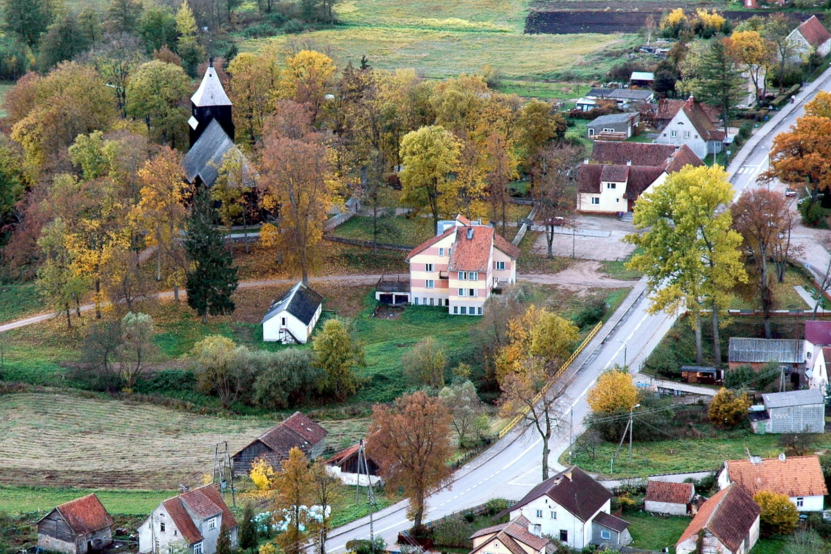 Widoczne są domy i kościół wśród drzew.