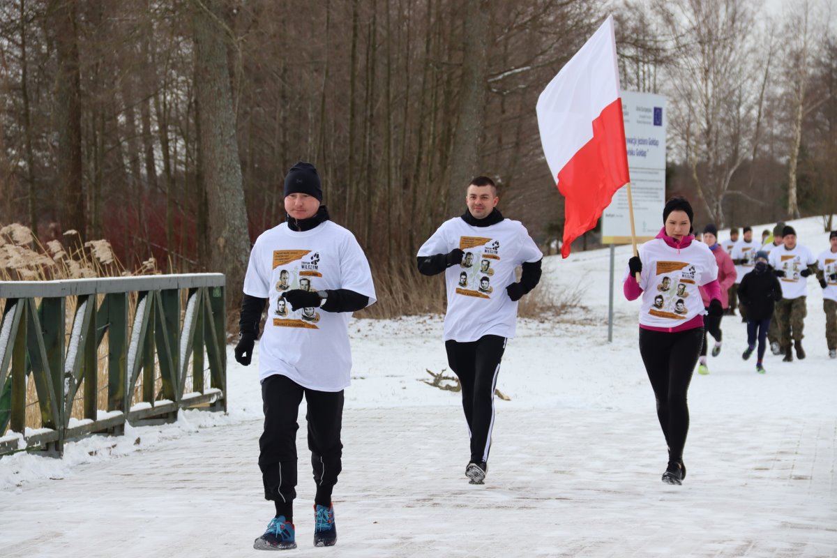 Kilku zawodników w czasie biegu. Jeden z nich trzyma flagę Polski.