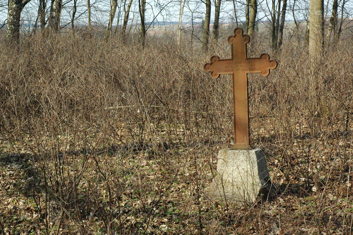 Krzyż żeliwy na nagrobku wśród drzew.