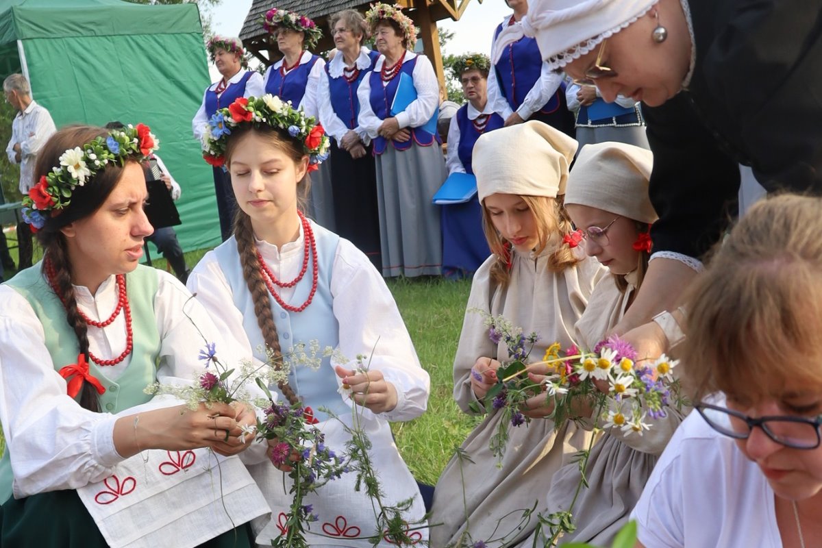 Grupa kobiet w ludowych strojach przy układaniu kwiatów.