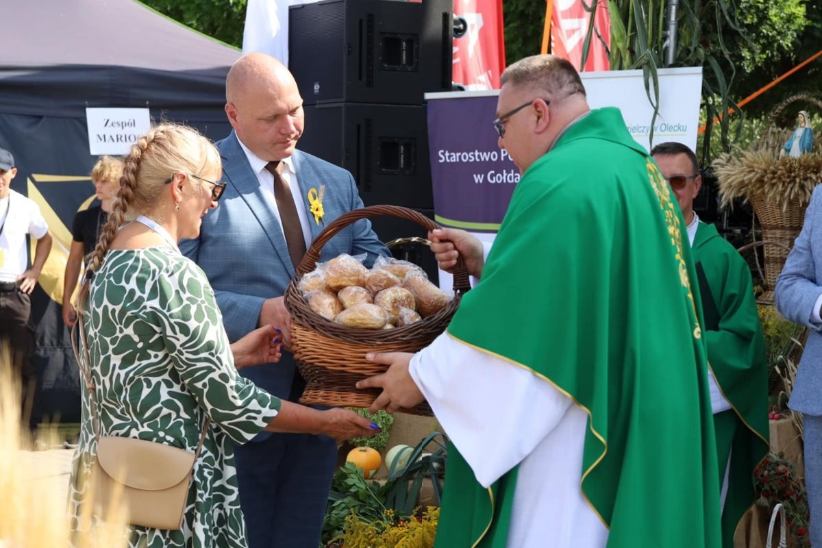 Kobieta i mężczyzna składają dary w czasie uroczystości. Po prawej stronie ksiądz.