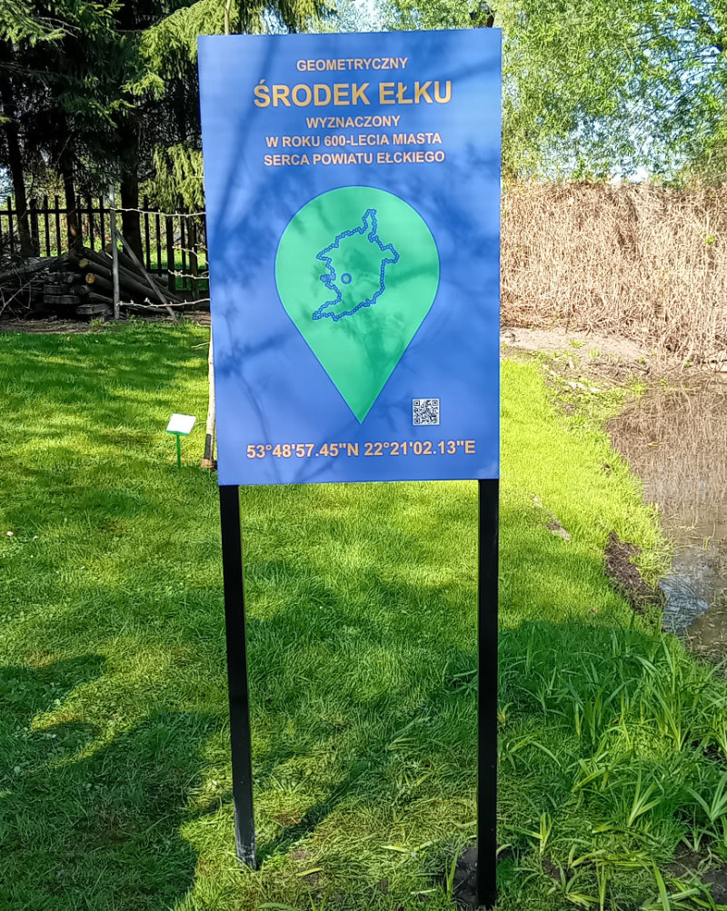 Na tle zieleni baner z napisem: Geometryczny środek Ełku.
