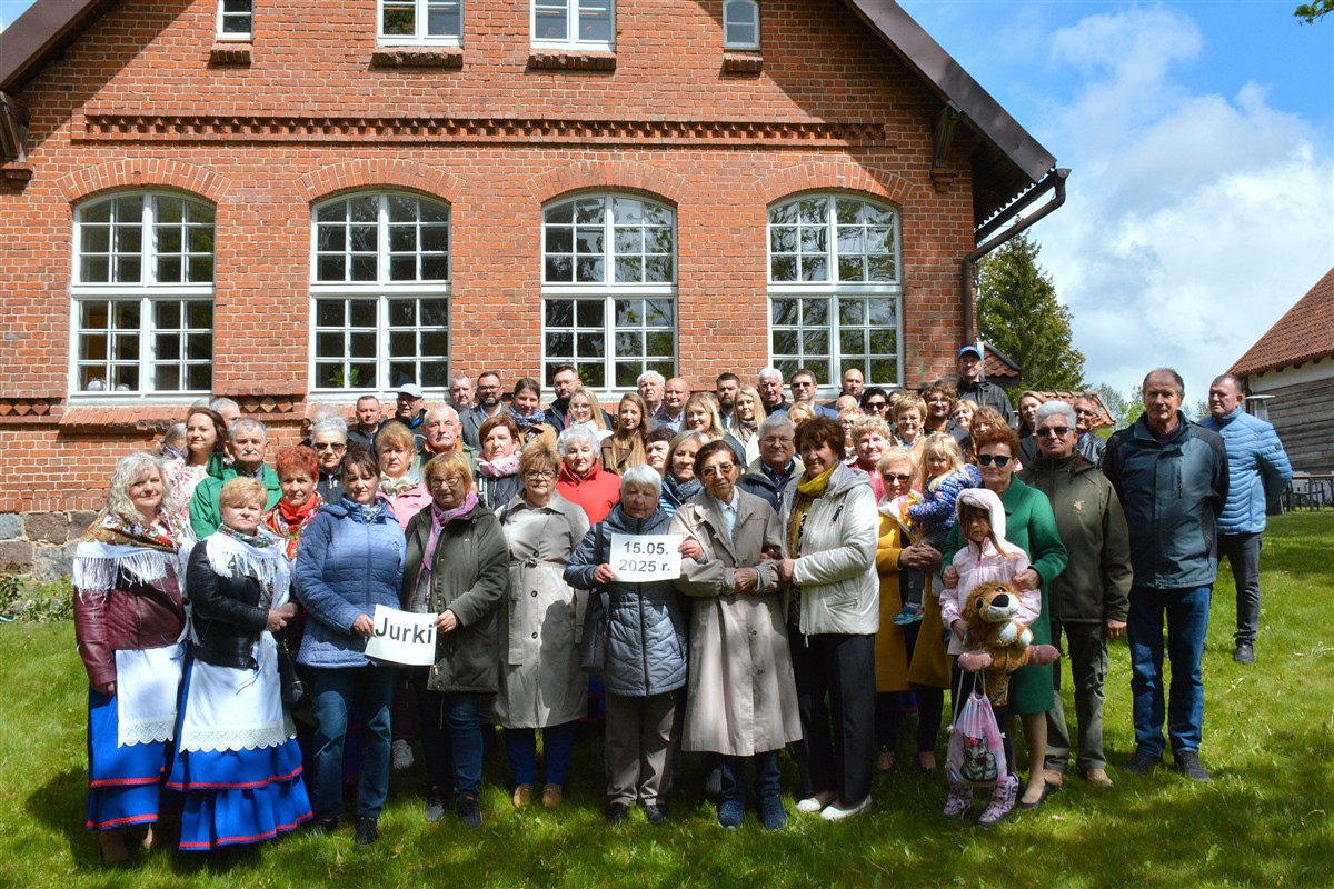 Duża grupa ludzi stoi przed ceglanym budynkiem, dwie kobiety trzymają tabliczki z napisem 