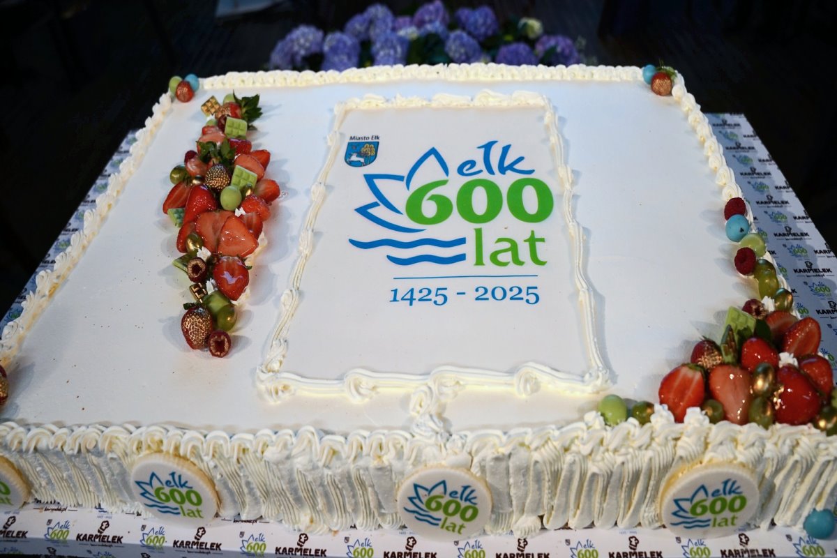 Duży biały tort z ozdobami z owoców i napisem „Ełk 600 lat 1425–2025”. Na torcie znajduje się także herb miasta Ełk i kolorowe dekoracje.