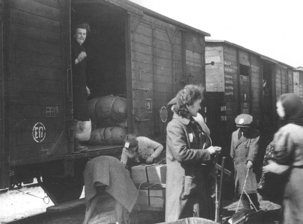 Ludzie z bagażami wsiadający do wagonu towarowego – scena przesiedlenia.