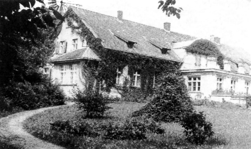 Czarno-białe zdjęcie zabudowań wiejskich z wiatrakiem w tle.