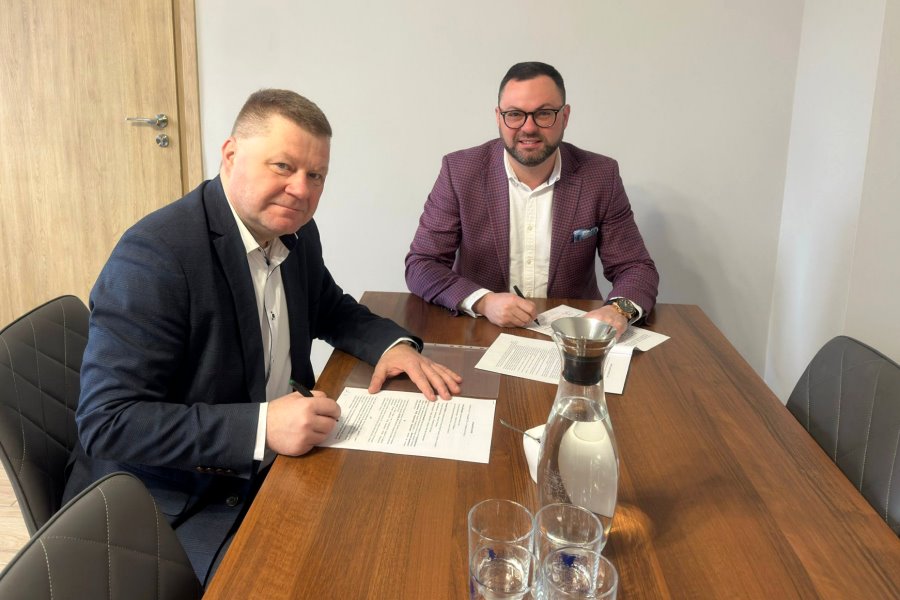 Dw&oacute;ch mężczyzn siedzi przy stole i podpisuje dokument.