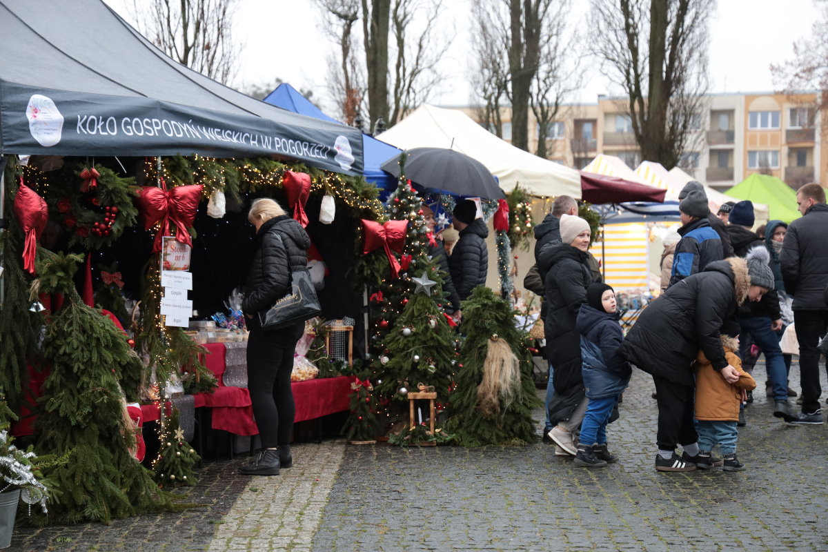 Stoisko świąteczne na jarmarku bożonarodzeniowym, przy kt&oacute;rym stoją odwiedzający.
