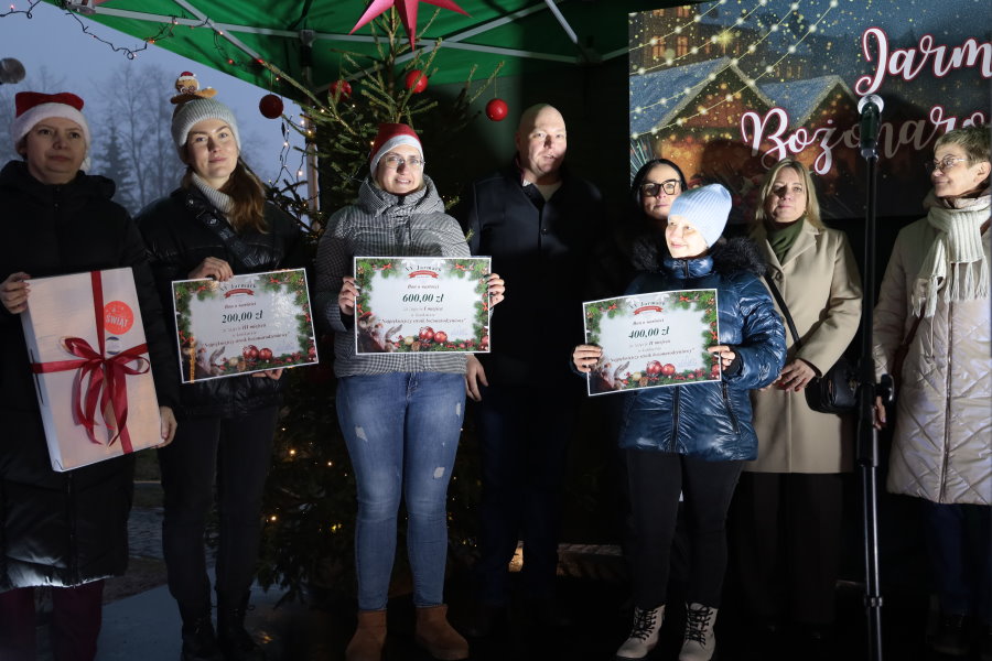 Grupa os&oacute;b na scenie podczas wydarzenia świątecznego, trzymających dyplomy lub nagrody.