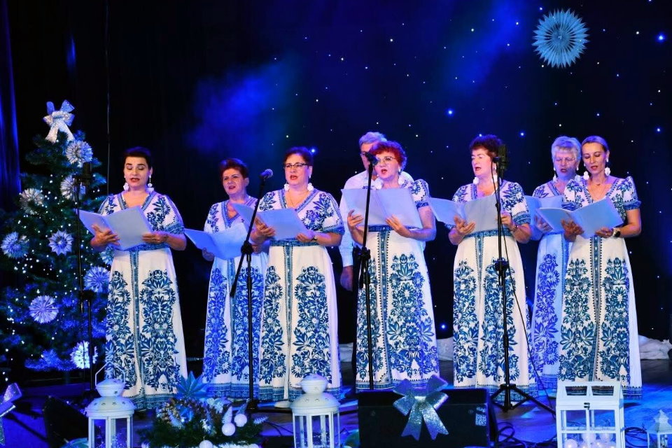 Zesp&oacute;ł ludowy w tradycyjnych strojach śpiewający na scenie przy choince.