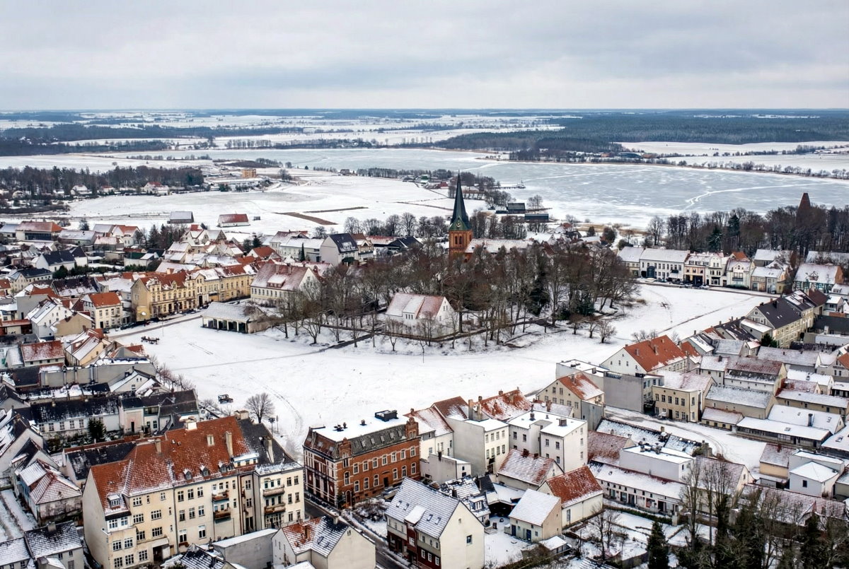 Lotniczy widok miasta Treuburg z 1930 roku zimą, zabudowa miejska pokryta śniegiem, widoczne jeziora i krajobraz wok&oacute;ł miasta.