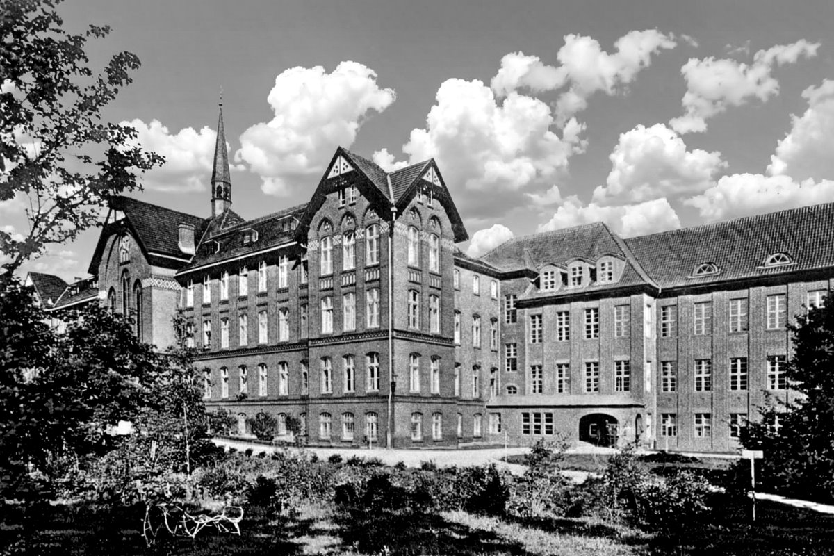 Czarno-biała fotografia historycznego szpitala w Lotzen, rozległy budynek z wieloma skrzydłami i ozdobnymi dachami.