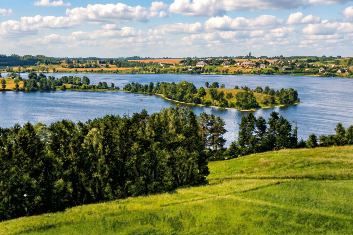 Krajobraz okolic Sensburga, zielone wzg&oacute;rza i jezioro otoczone drzewami, widok panoramiczny.