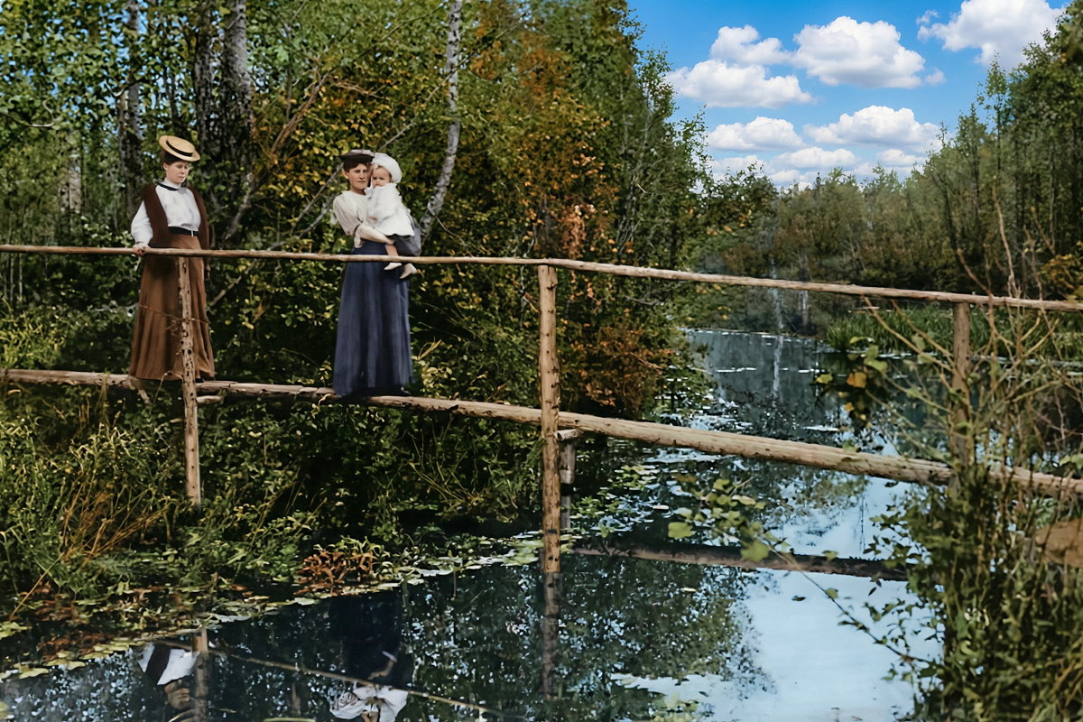 Drewniany mostek nad wodą wśród drzew, na którym stoją ludzie podziwiający przyrodę