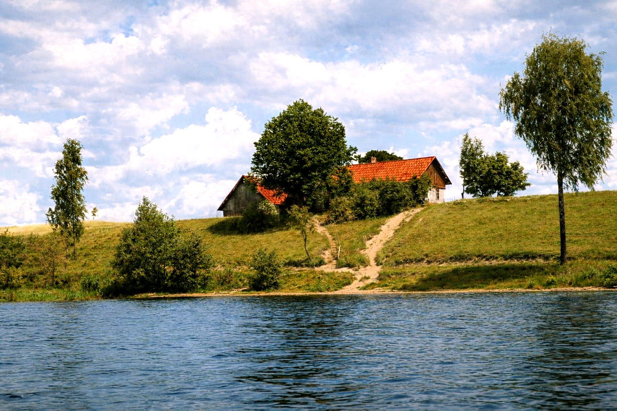 Widok na jezioro i zielony półwysep z zabudową w oddali, pod błękitnym niebem z rozproszonymi chmurami.