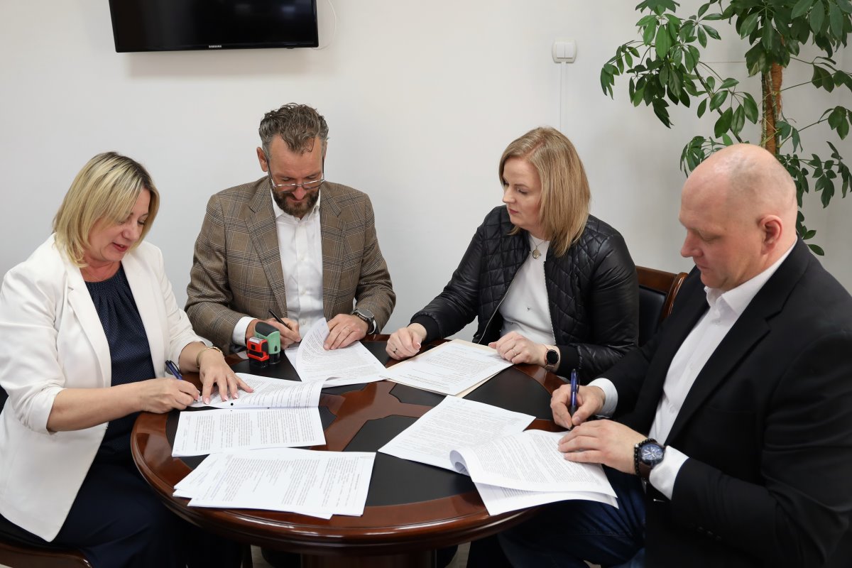 Cztery osoby podpisują dokumenty przy okrągłym stole w biurze podczas formalnego spotkania biznesowego.