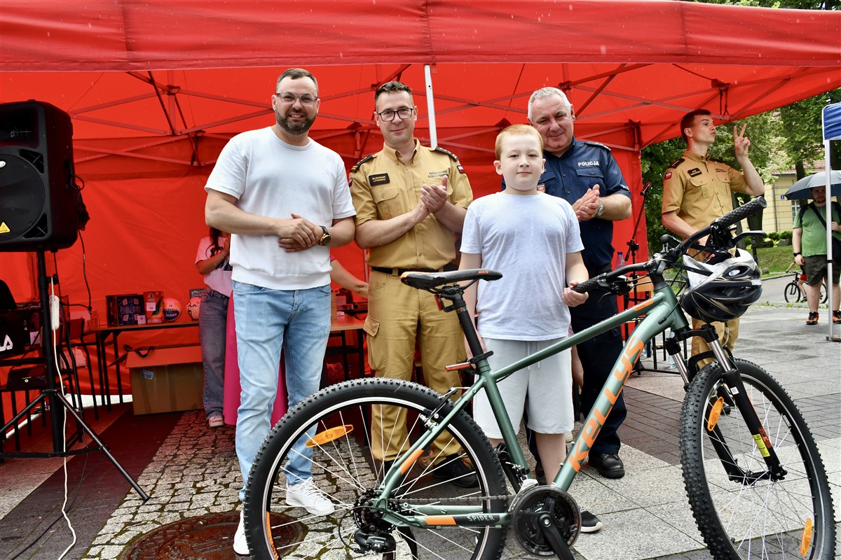 Chłopiec stoi obok nowego roweru otrzymanego jako nagroda i pozuje do zdjęcia z organizatorami oraz funkcjonariuszami podczas ceremonii wręczenia.