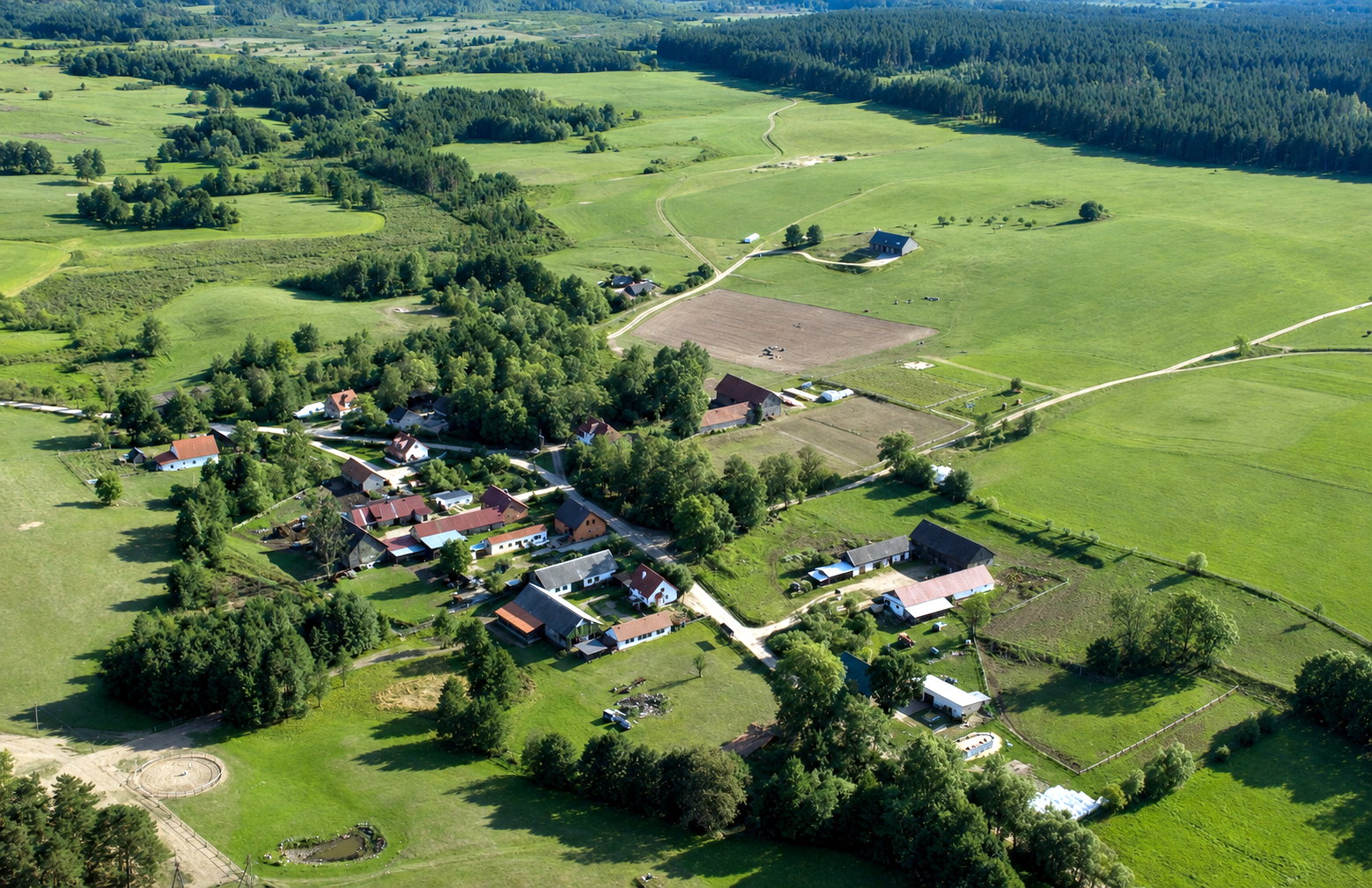 Zdjęcie lotnicze ukazuje centrum miejscowości Bachort z zabudową gospodarczą, drogami oraz rozległymi terenami rolniczymi otaczającymi wieś w letnim krajobrazie.