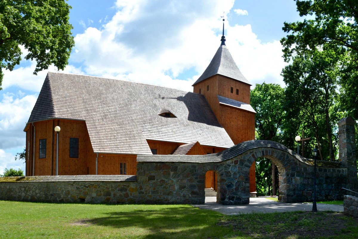 Widok na drewniany kości&oacute;ł Narodzenia Najświętszej Maryi Panny w Wieliczkach z kamienną bramą prowadzącą na teren przykościelny. Stan z 2026 roku.