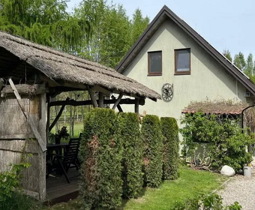 Widok na dom otoczony zielenią. Po lewej stronie szopa dreweniana.